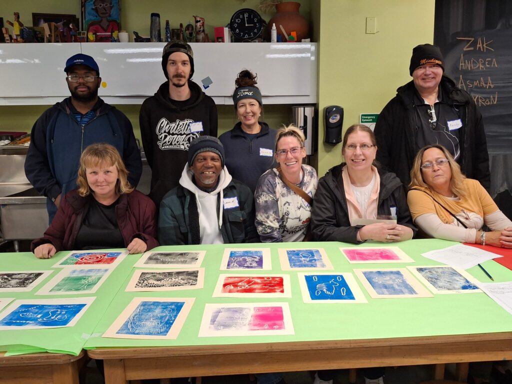 Liberties Inc. DIA Visit A diverse group of smiling individuals sitting and standing together in front of vibrant artwork prints.